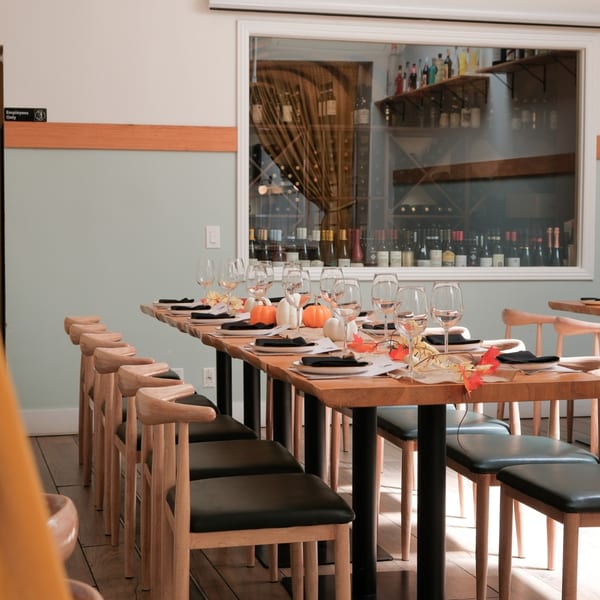 A long wooden dining table set with plates, wine glasses, and pumpkin decorations, in a restaurant.