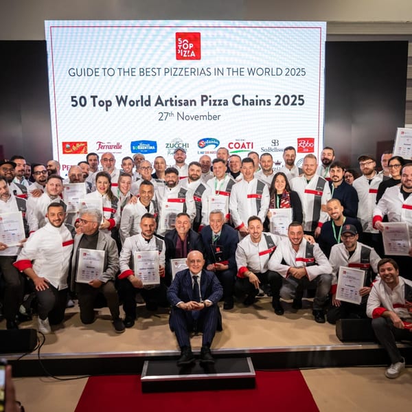 A large group of chefs and restaurateurs pose with awards in front of a screen displaying "50 Top Pizza".