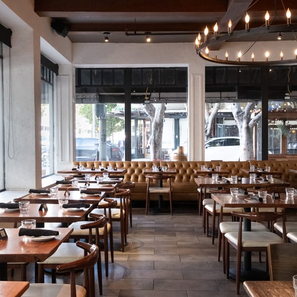 Doppio Zero's dining room with wooden tables, brown leather banquettes, and large street-facing windows.