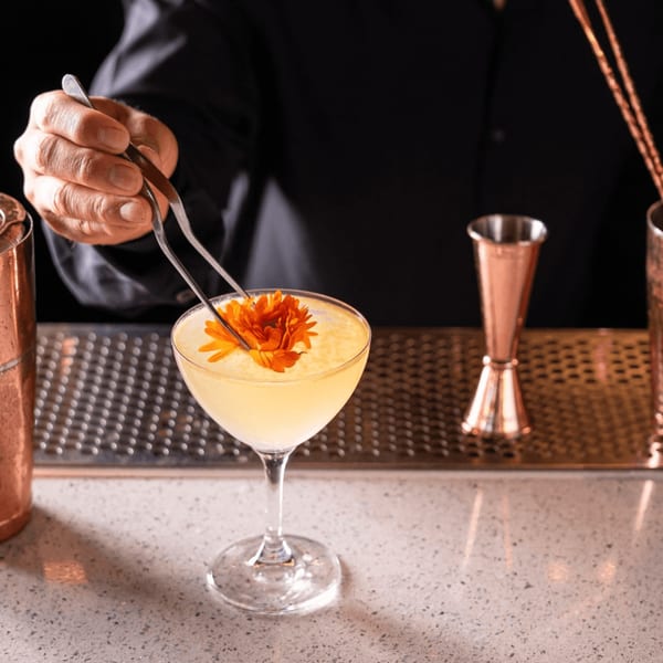 Bartender garnishing a yellow cocktail with an orange flower using tweezers at Doppio Zero.