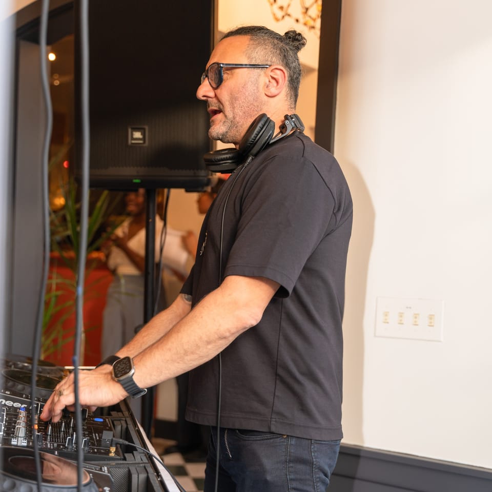 A DJ with headphones around his neck, wearing glasses and a black shirt, mixing music.
