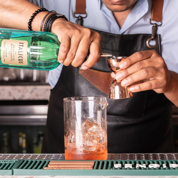 Bartender pouring Italicus Rosolio di Bergamotto liqueur into a jigger over a glass with ice.