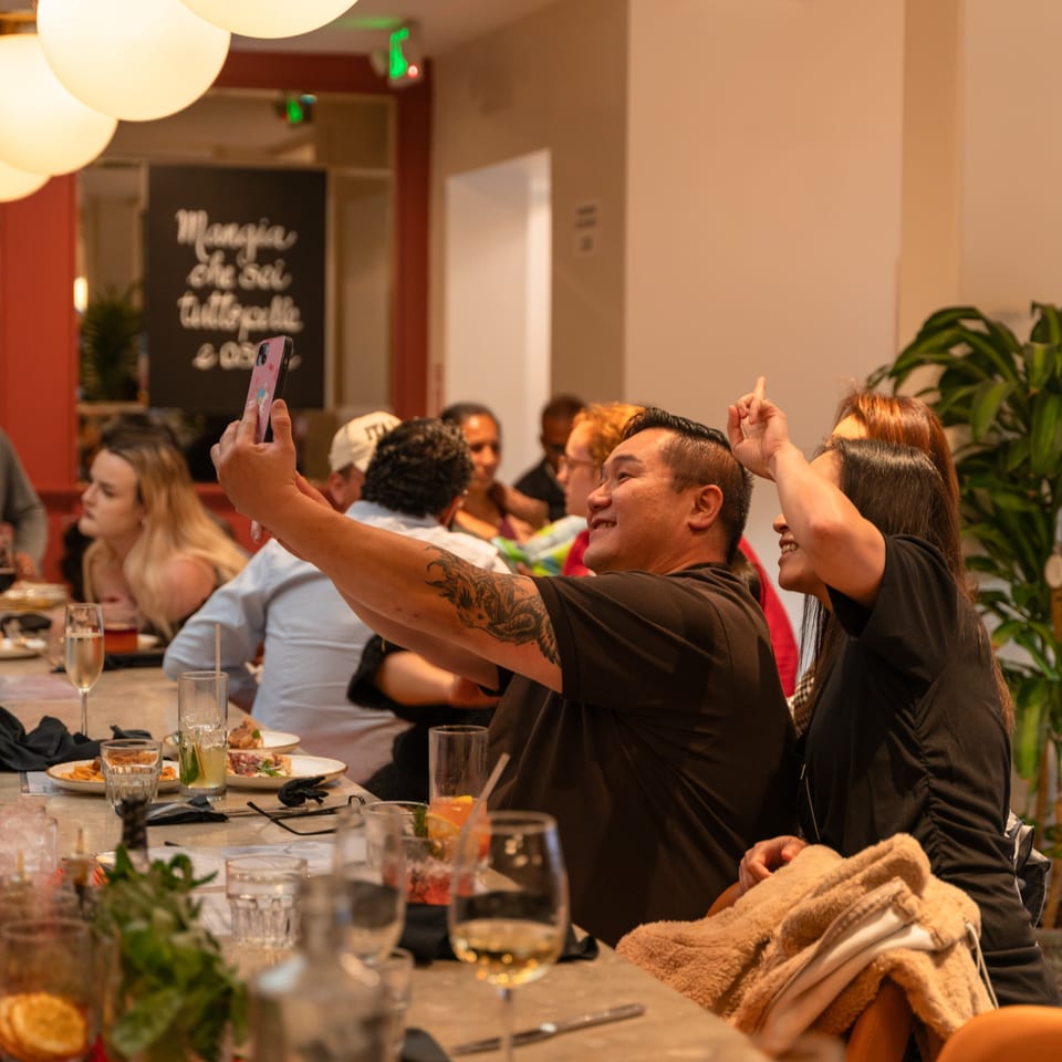 Two people taking a selfie at a long dining table filled with food and drinks.