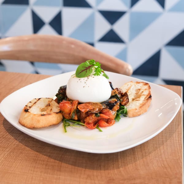 Burrata cheese with roasted vegetables, arugula, and grilled bread on a white plate.