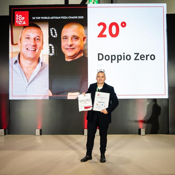 A man holding two awards for Doppio Zero, standing before a large screen displaying "50 Top World Artisan Pizza Chains 2025".