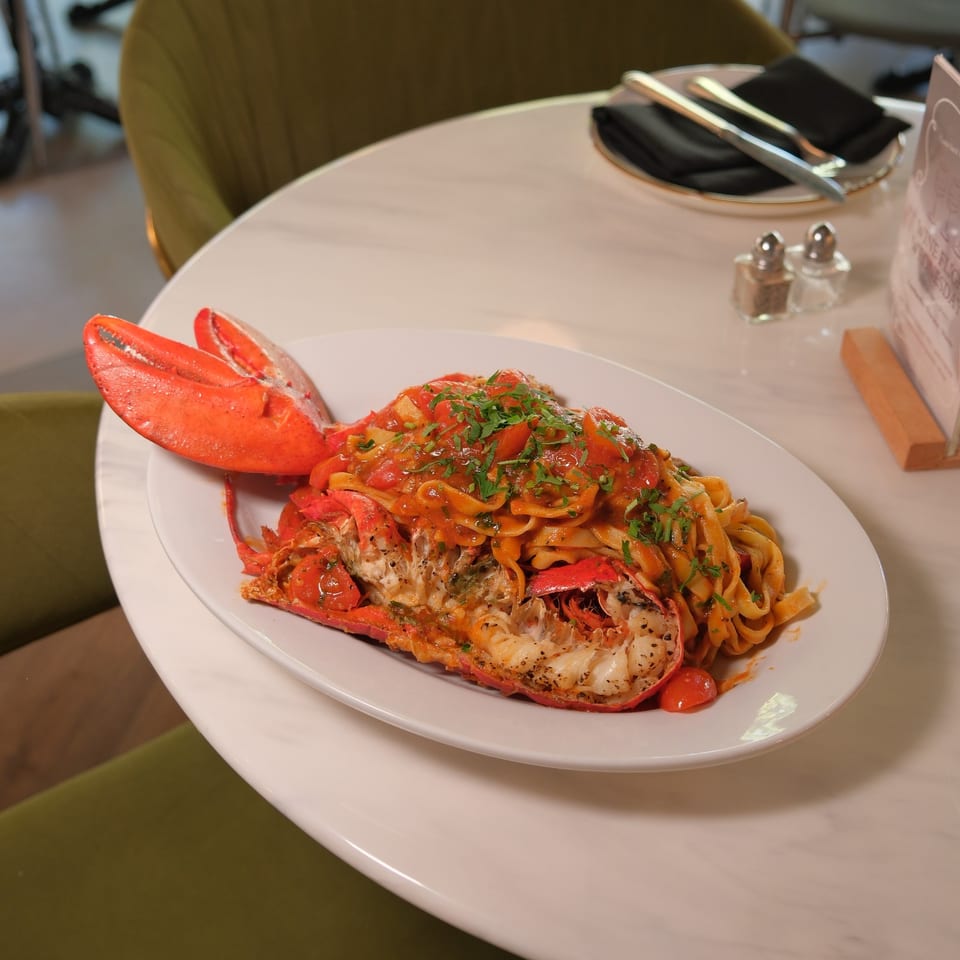 Lobster pasta with tomato sauce and fresh herbs served on a white plate at a restaurant table.