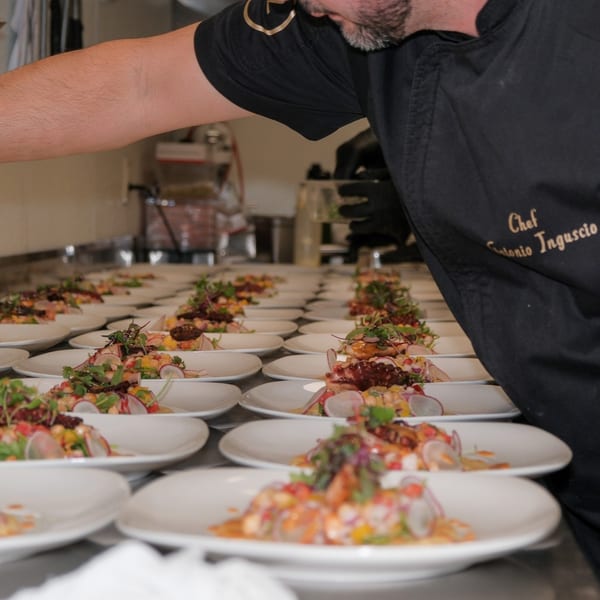 Chef Antonio Inguscio plating rows of colorful seafood salads with microgreens in a professional kitchen.