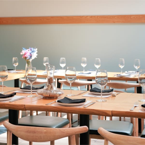 Set tables with wine glasses, black napkins, and a decanter filled with corks in a restaurant.