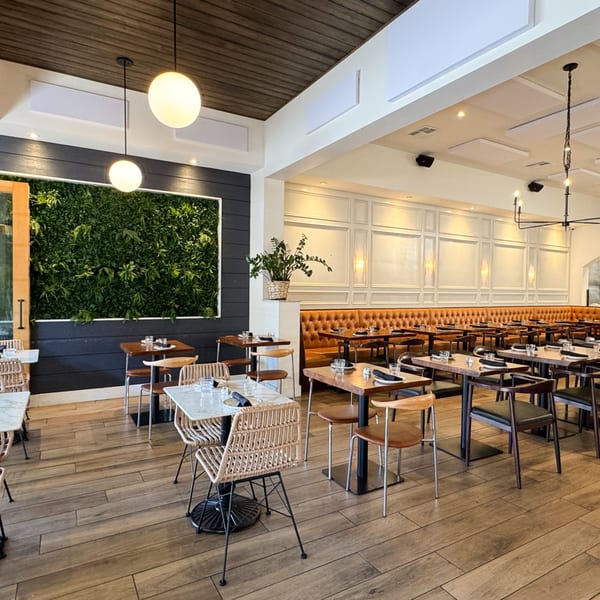 Modern restaurant interior with a green wall, wooden floors, and tables with brown leather banquettes.