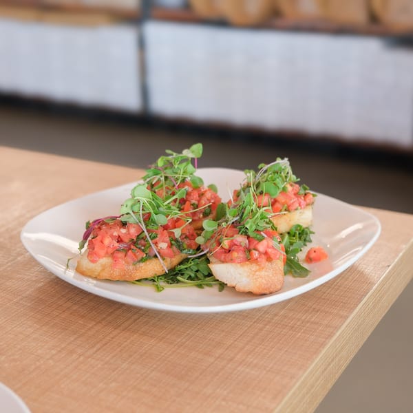 Doppio Zero's bruschetta with diced tomatoes, herbs, and microgreens on a white plate.