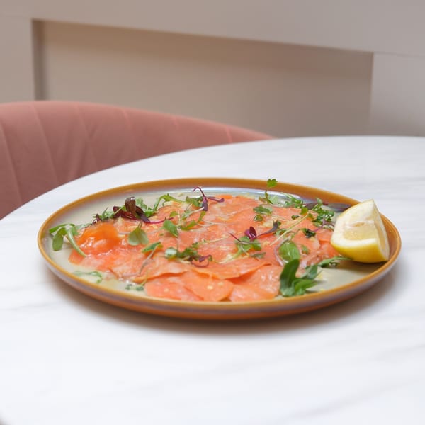 Doppio Zero's salmon carpaccio, garnished with microgreens and a lemon wedge, on a white table.