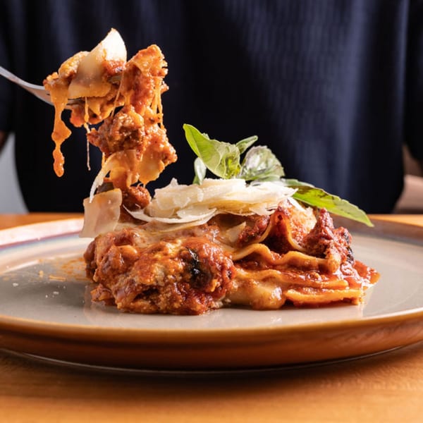 A fork lifts a cheesy, saucy bite of lasagna from a plate garnished with basil and parmesan.